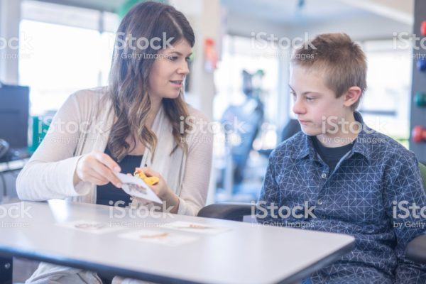istockphoto-1074803012-2048x2048 A female speech therapist works with a handsome elementary-age boy in a clinic setting. They are organizing alphabet cards on the table together.